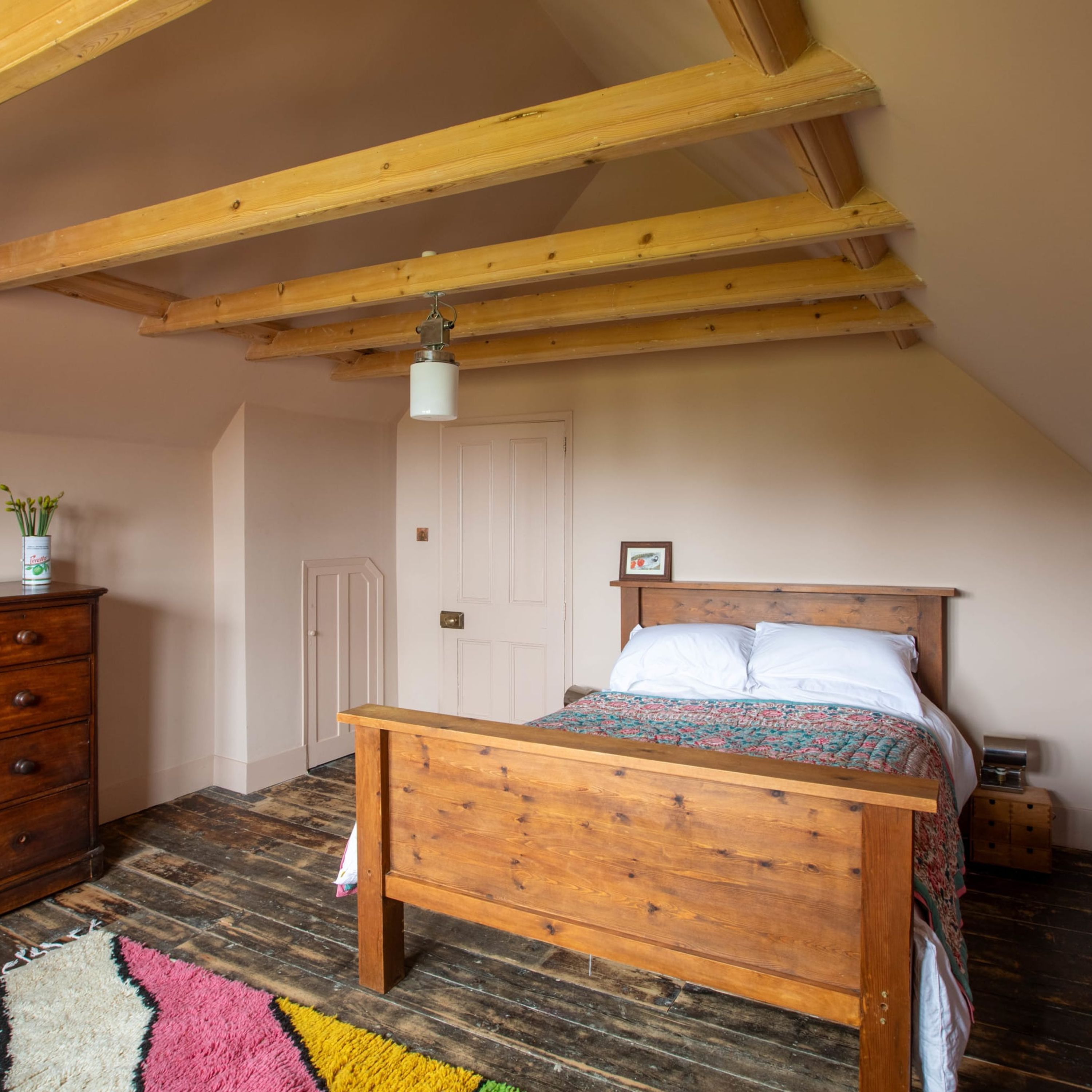 A bedroom with a wooden bed, a dresser, a nightstand, a lamp, and a door.