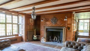 A spacious living room with a fireplace, leather sofas, and a guitar. - Large Country House in Ashdown Forest (East Grinstead)