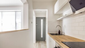 A narrow kitchen with a wooden countertop, white tiled backsplash, and a grey door. - Light-filled Studio With AC - Earl s Court (London)