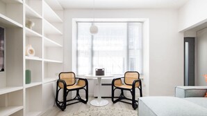 A modern room with white walls, a round table, two wicker chairs, a hanging light, and a window with blinds. - Light-filled Studio With AC - Earl s Court (London)