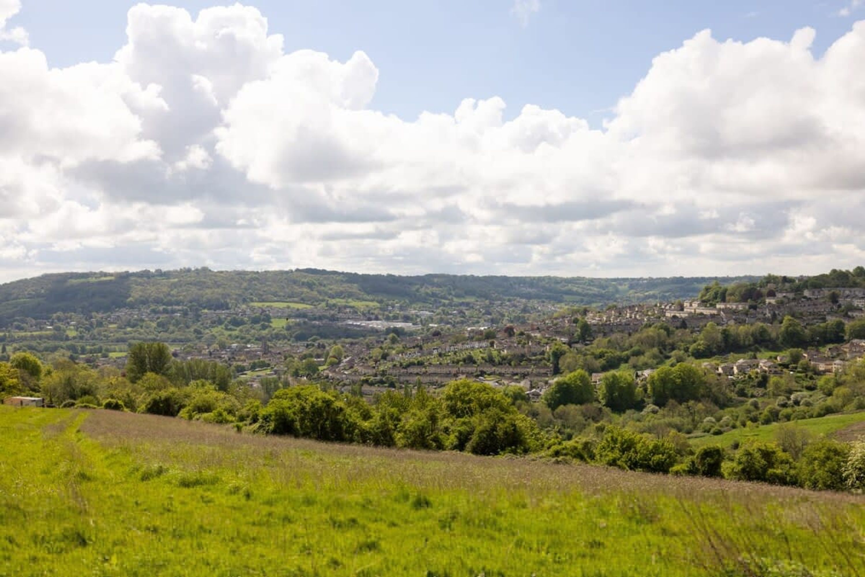 Ländliche Landschaft mit sanften Hügeln, einem Dorf in der Ferne und wolkenlosem Himmel.