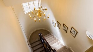 Eine Treppe mit einer Chandelüstere, gerahmten Bildern an der Wand und einem Fenster.