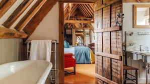 Une chambre à coucher rustique avec un plafond en bois, un lit recouvert d’une courtepointe bleue et jaune, et une armoire en bois dotée d’un miroir.