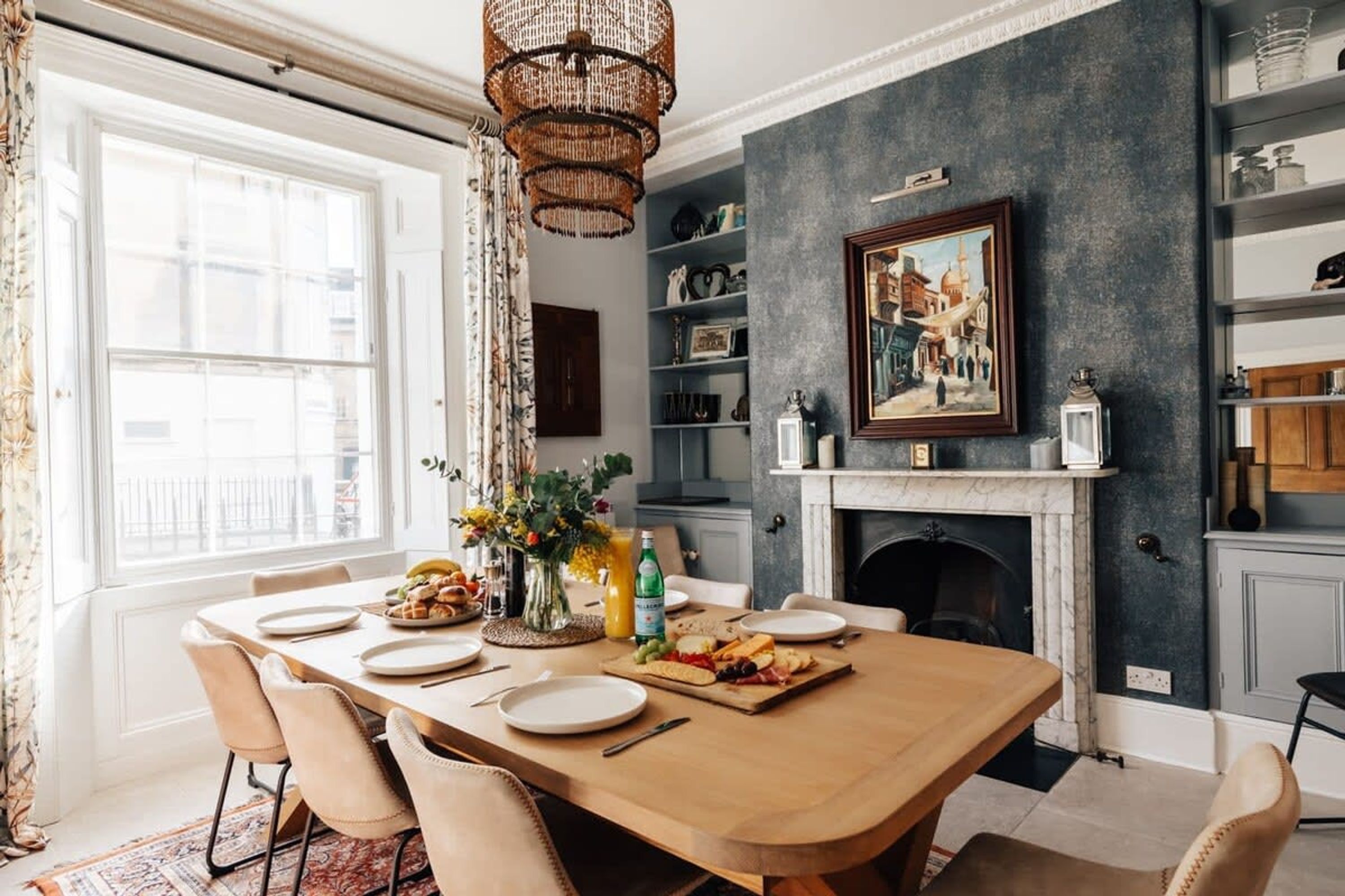 A dining area with a large wooden table, chairs, a chandelier, and a fireplace.