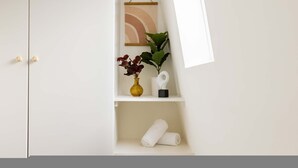 Une armoire blanche avec une étagère où sont posés un vase de fleurs, un tableau encadré et une serviette enroulée.