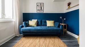 Une pièce avec un canapé bleu, un tapis tissé, un tableau encadré accroché au mur et une petite table avec une lampe.