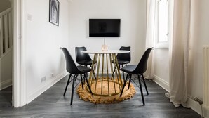 Un coin repas avec une table ronde, quatre chaises, un téléviseur à écran plat fixé au mur et une fenêtre avec des rideaux.