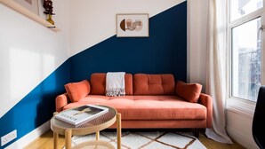 Ein Wohnzimmer mit einem pfirsichfarbenen Sofa, einem runden Couchtisch mit einer Zeitschrift, einem gerahmten abstrakten Kunstwerk und einem Fenster mit Vorhängen.