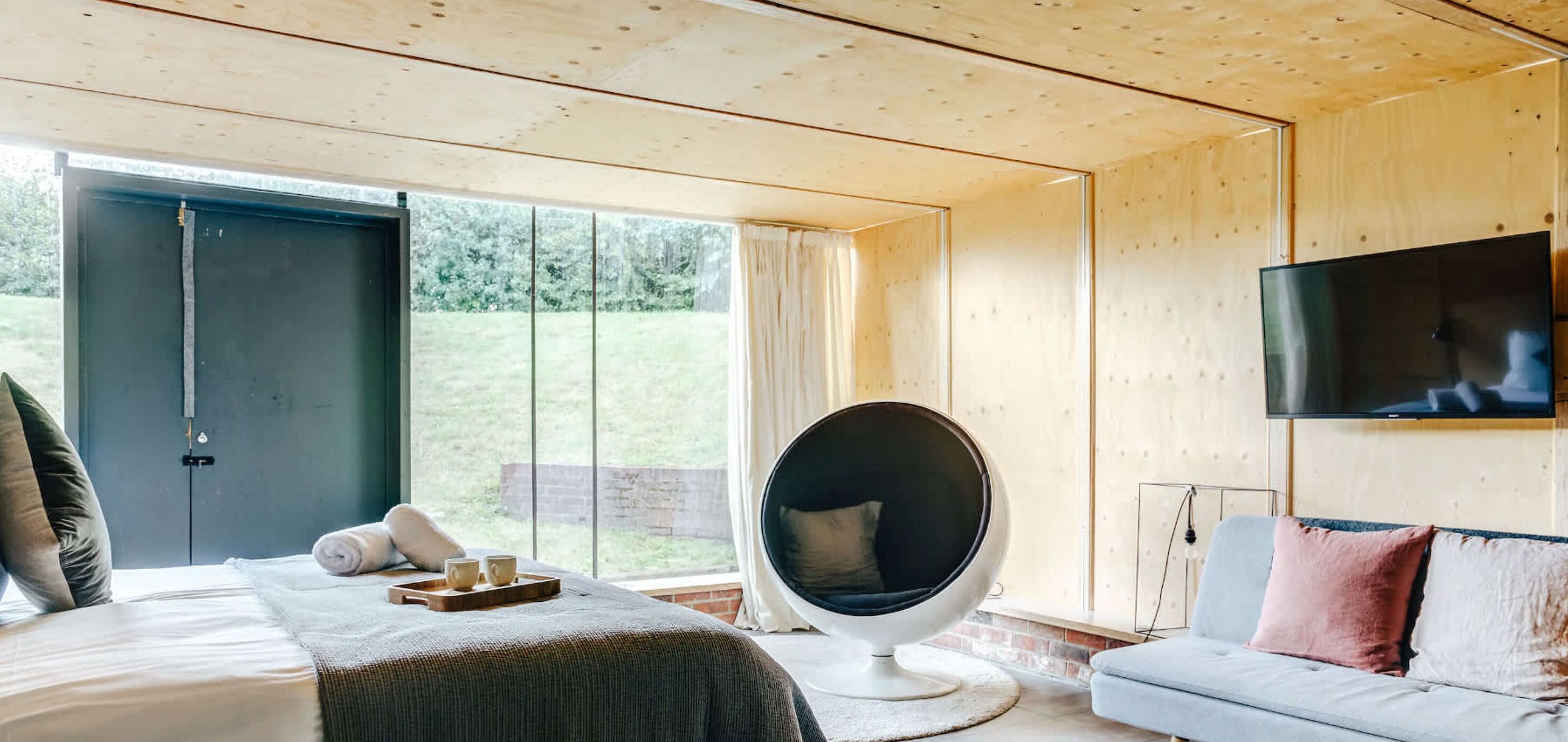 Une chambre à coucher moderne avec un lit, un canapé, une grande fenêtre et un téléviseur.