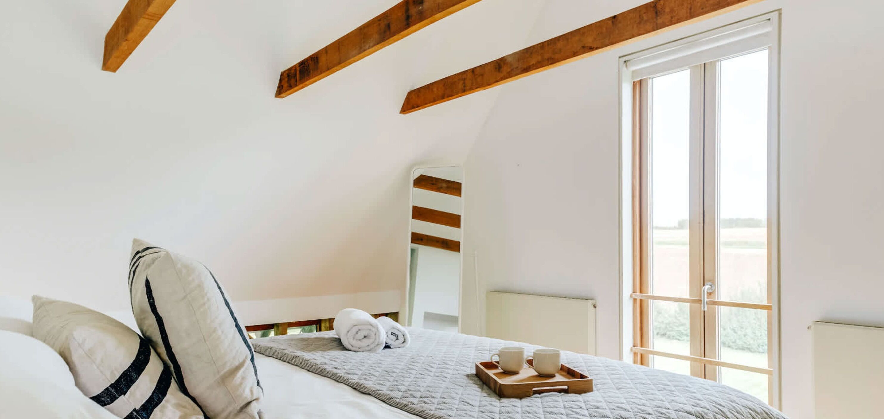 Una camera da letto con un letto, cuscini, un comodino con due tazze e una finestra vista.