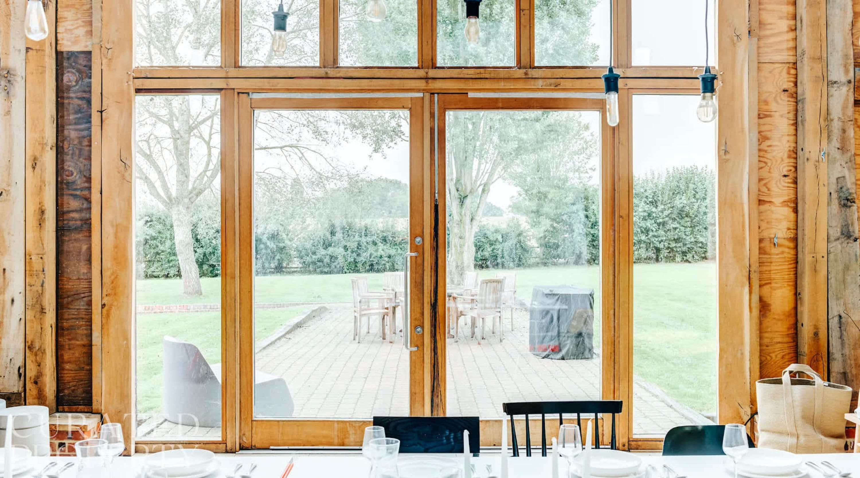 Interior de madera con amplios ventanales que dan a un patio exterior con sillas y una mesa lista para comer.