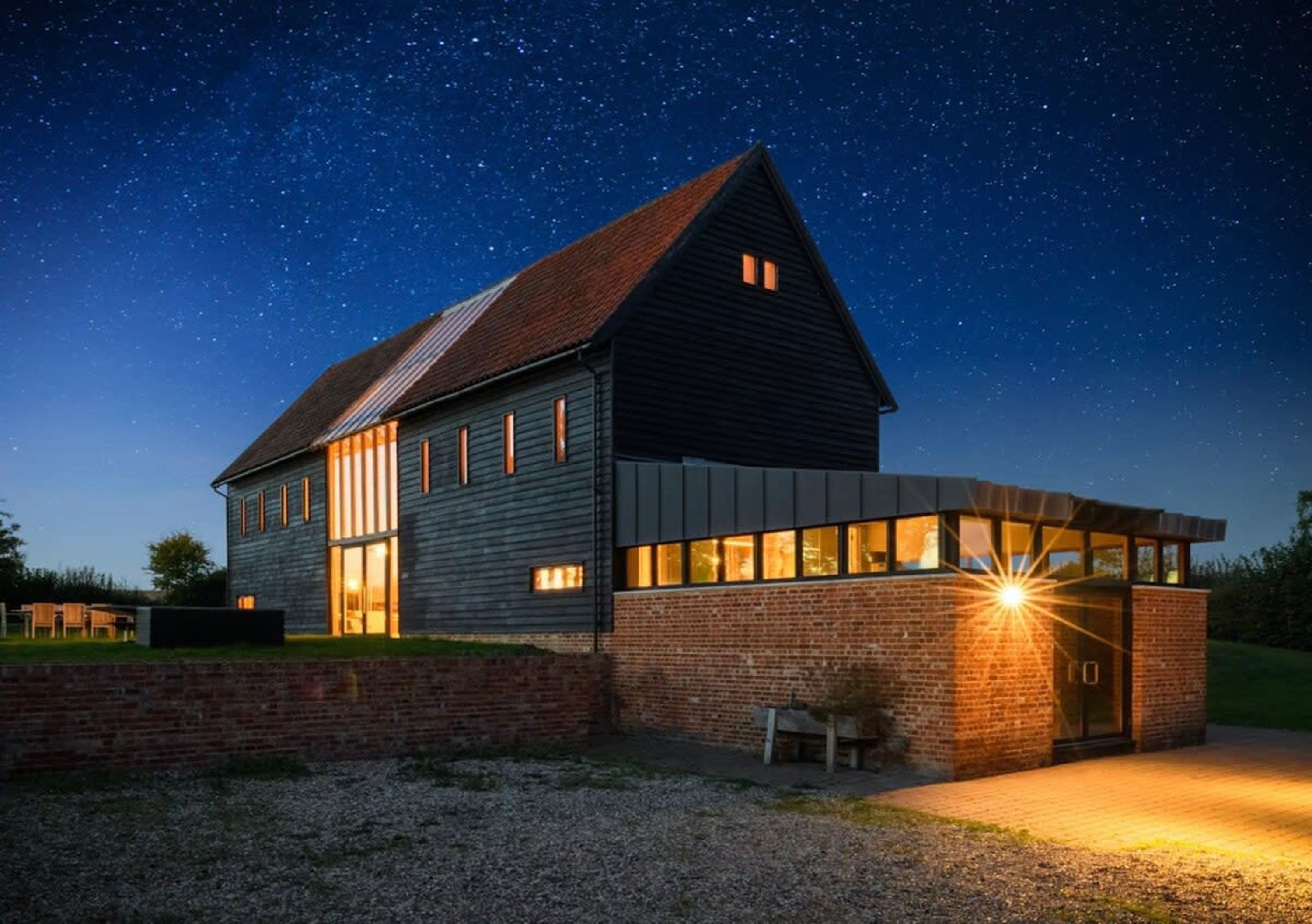 A modern house with a sloped roof and large windows, set against a night sky with stars.