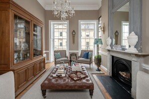 A traditional living room with a large wooden cabinet, a leather ottoman, two armchairs, a chandelier, and a fireplace. - Former Prime Minister s Home (Bath)