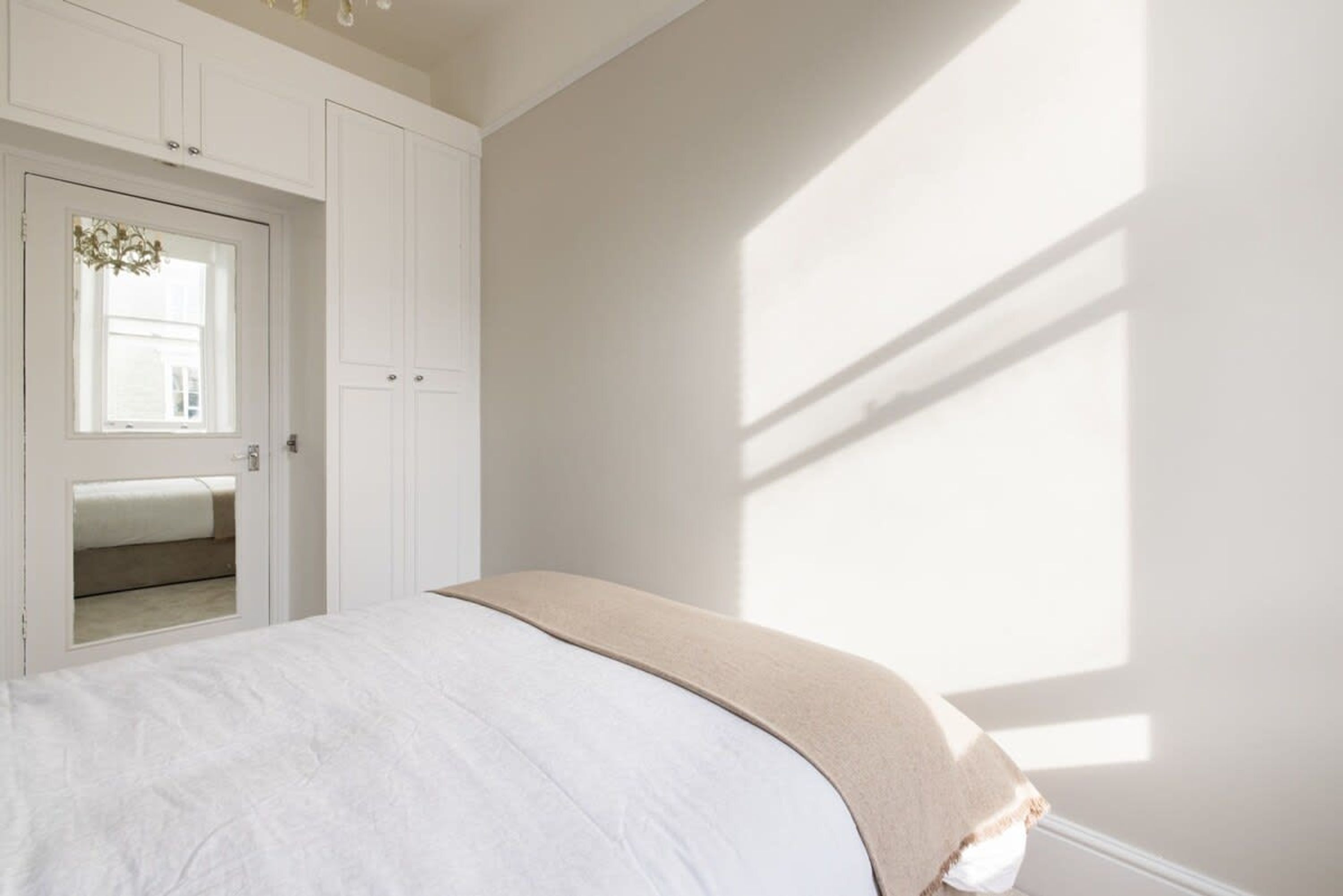 A bedroom with a bed, a wardrobe, and a window casting shadows.