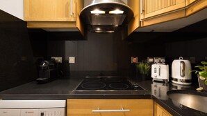 A modern kitchen with wooden cabinets, a Bosch dishwasher, a black countertop, and a stainless steel range hood. - Chic Sunlit Earls Court Flat (London)