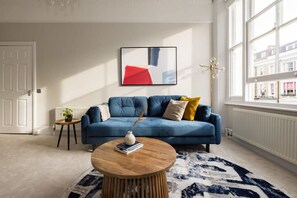 Un salon moderne avec un canapé bleu, une table basse ronde en bois et un grand tableau abstrait accroché au mur.