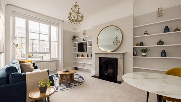 A living room with a sofa, a round coffee table, a fireplace, and a dining table. - Chic Sunlit Earls Court Flat (London)