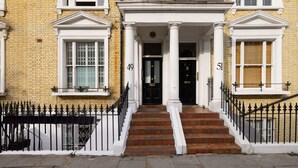 A two-story building with a brick facade, numbered doors, and a black iron fence. - Chic Sunlit Earls Court Flat (London)