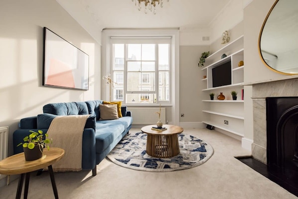 Un salon moderne avec un canapé bleu, une table basse ronde et une grande fenêtre.