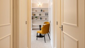 A hallway leading to a dining area with a round table and two yellow chairs. Shelves with various items line the walls. - Chic Sunlit Earls Court Flat (London)