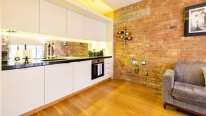 A modern kitchen with white cabinets, a brick wall, and a wooden floor. - Central Soho Loft With A C Concierge (London)