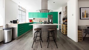 Une cuisine moderne avec des meubles de couleur verte, un îlot central doté de tabourets et une poubelle en acier inoxydable.
