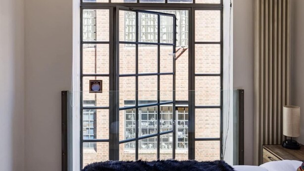 Une chambre d’hôtel avec une grande fenêtre, un radiateur et une table de chevet avec une lampe.
