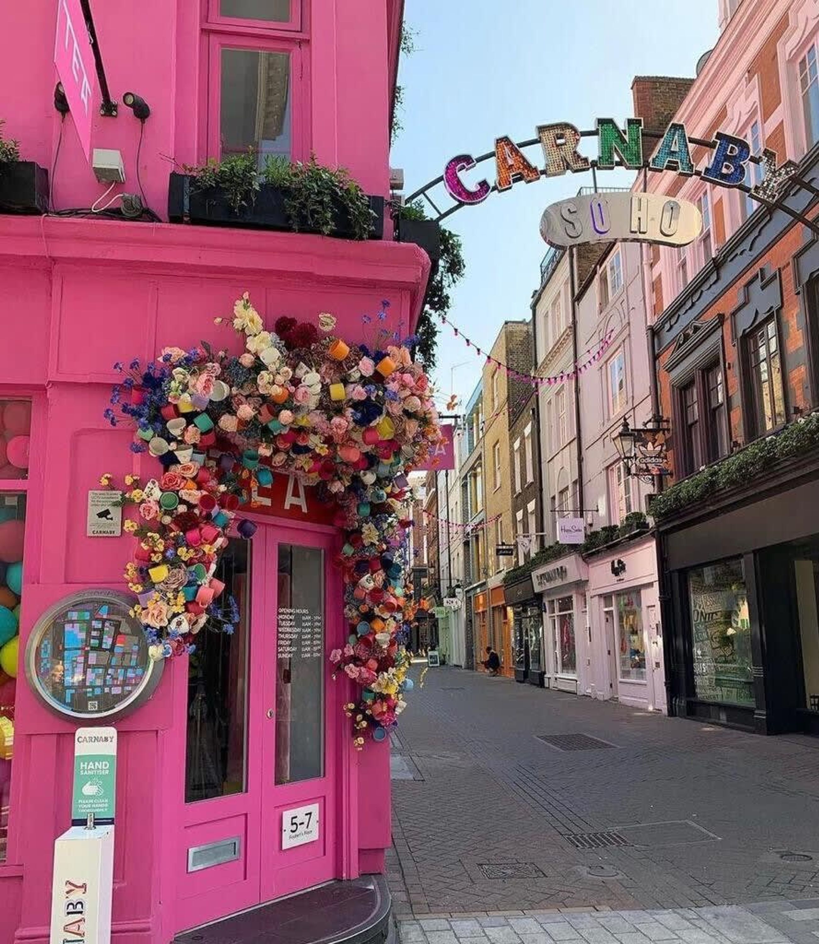 Ein pinkfarbenes Gebäude mit einem Schild, auf dem "Carnaby Soho" steht, und einer floralen Dekoration über dem Eingang.