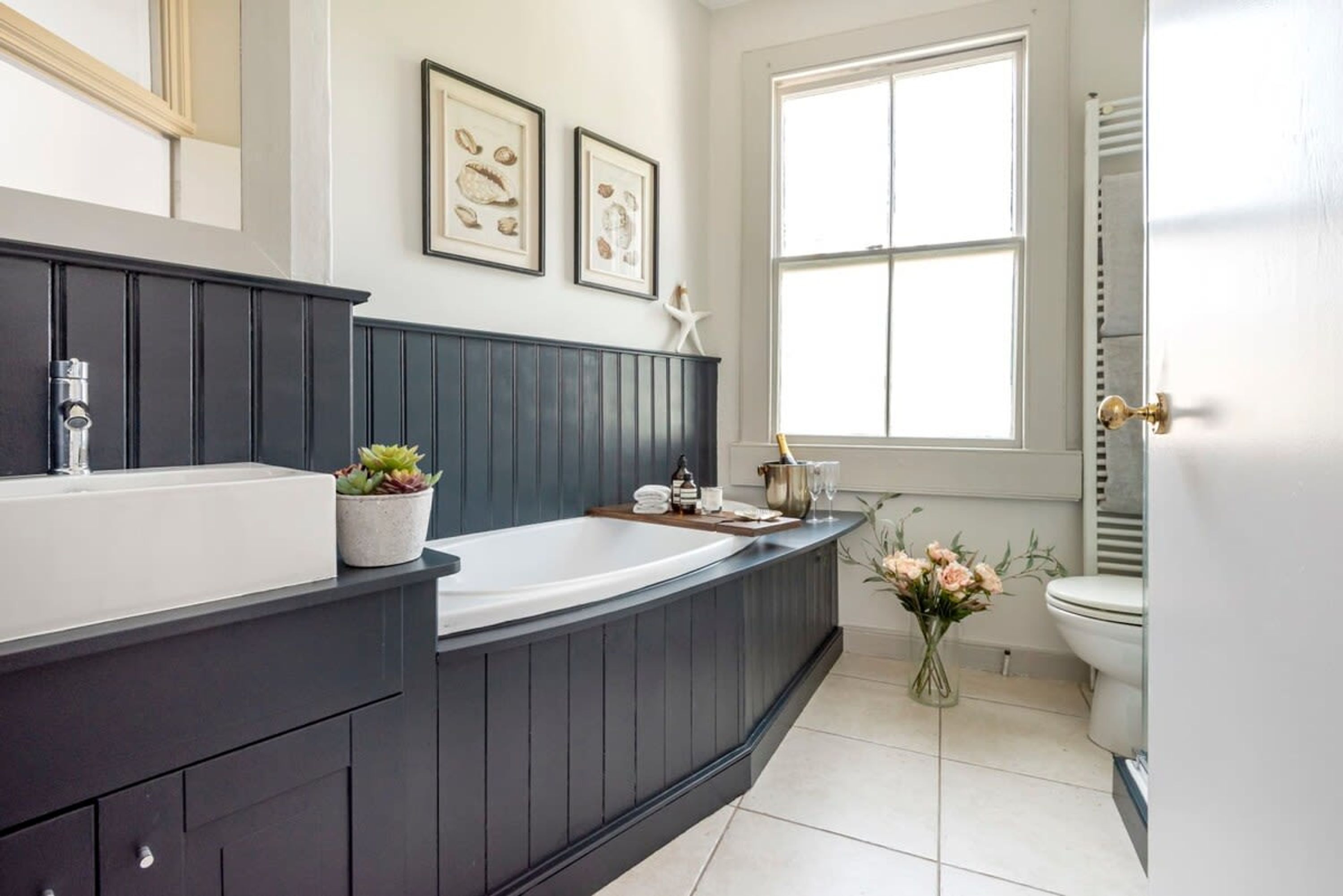 A modern bathroom with a dark wooden vanity, a large bathtub, and a window providing natural light.