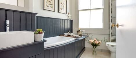 A modern bathroom with a dark wooden vanity, a large bathtub, and a window providing natural light.