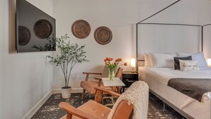 A bedroom with a four-poster bed, a small table with a vase of flowers, a chair, and a potted plant. - The Orenco Station Hotel (Hillsboro)