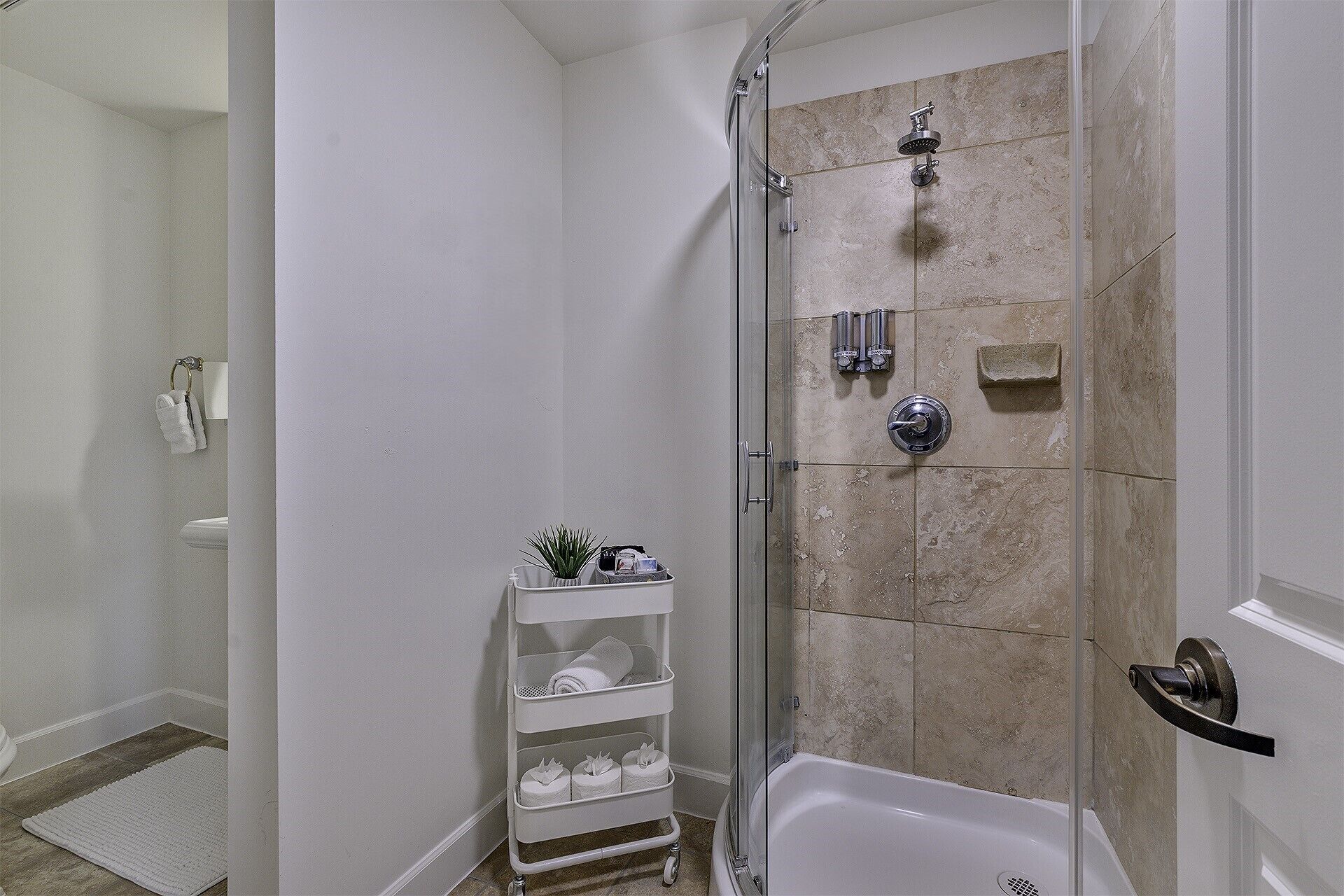 A shower with a glass door, a white bathtub, and a shelf with toiletries.