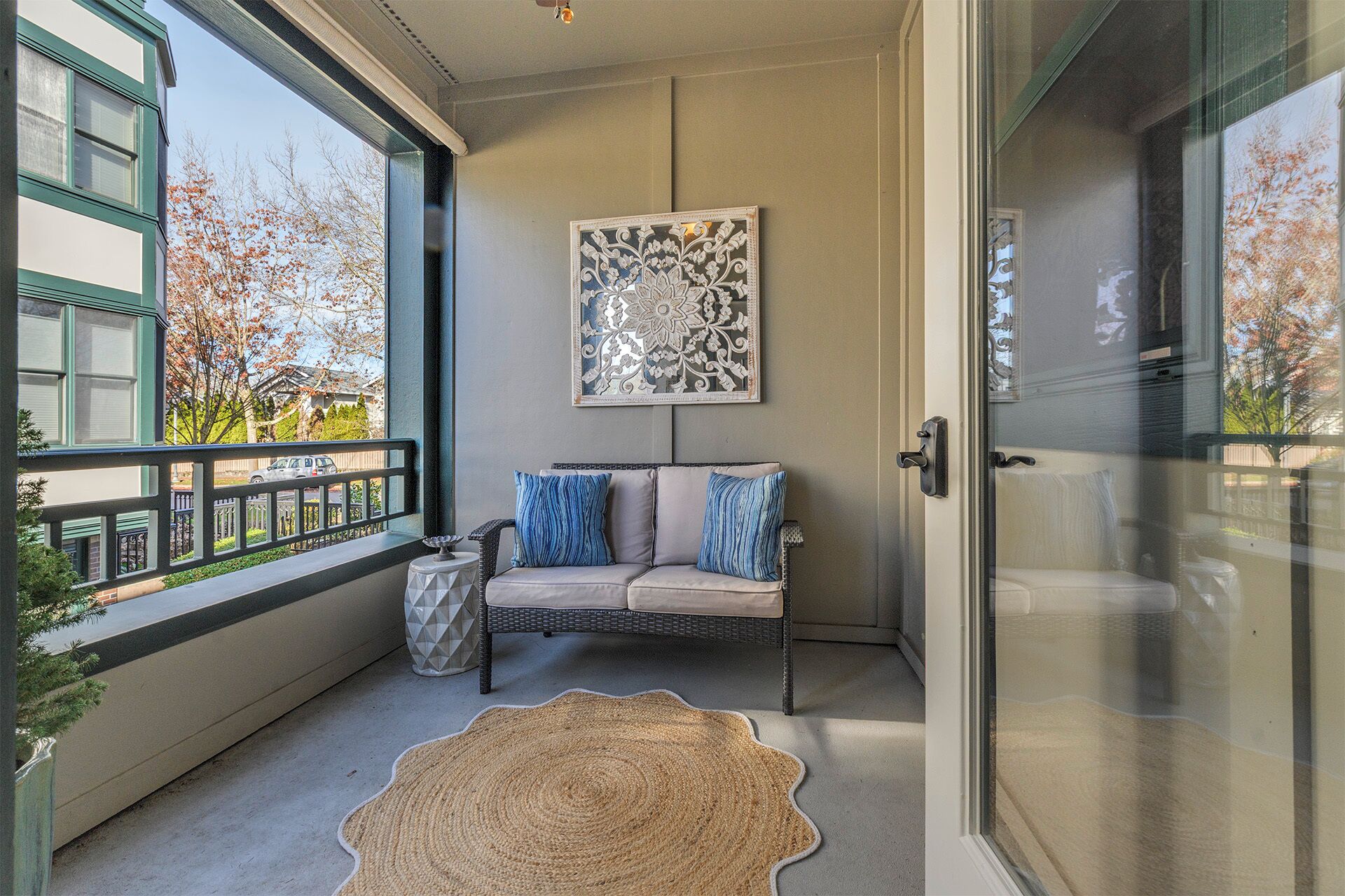 A balcony with a wicker sofa, a decorative rug, and a framed artwork.