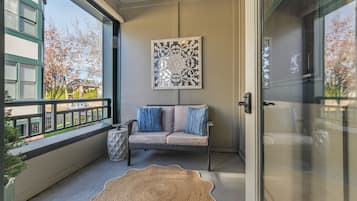 A balcony with a wicker sofa, a decorative rug, and a framed artwork.