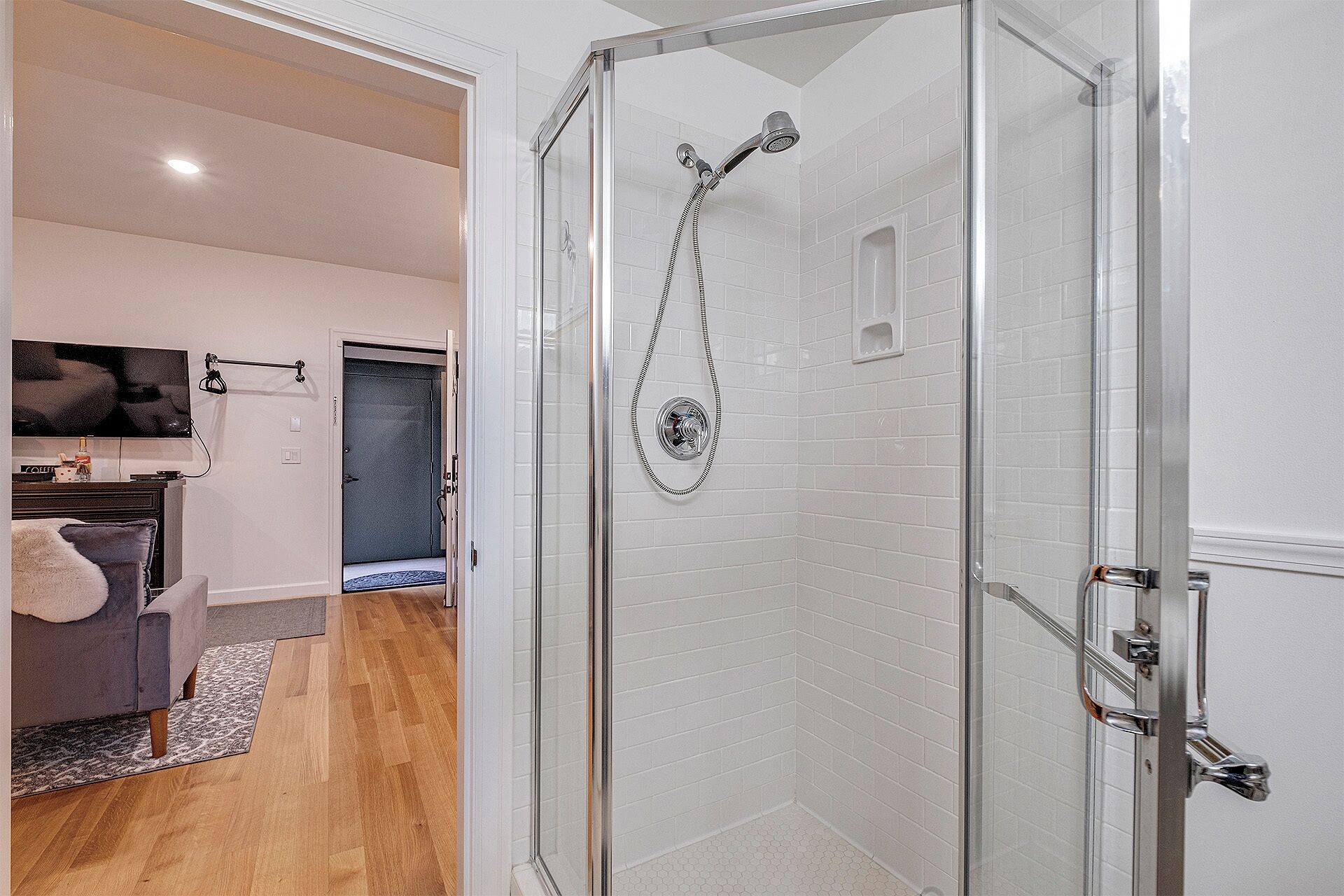 A modern bathroom with a glass shower enclosure, white tiled walls, and a wooden floor.