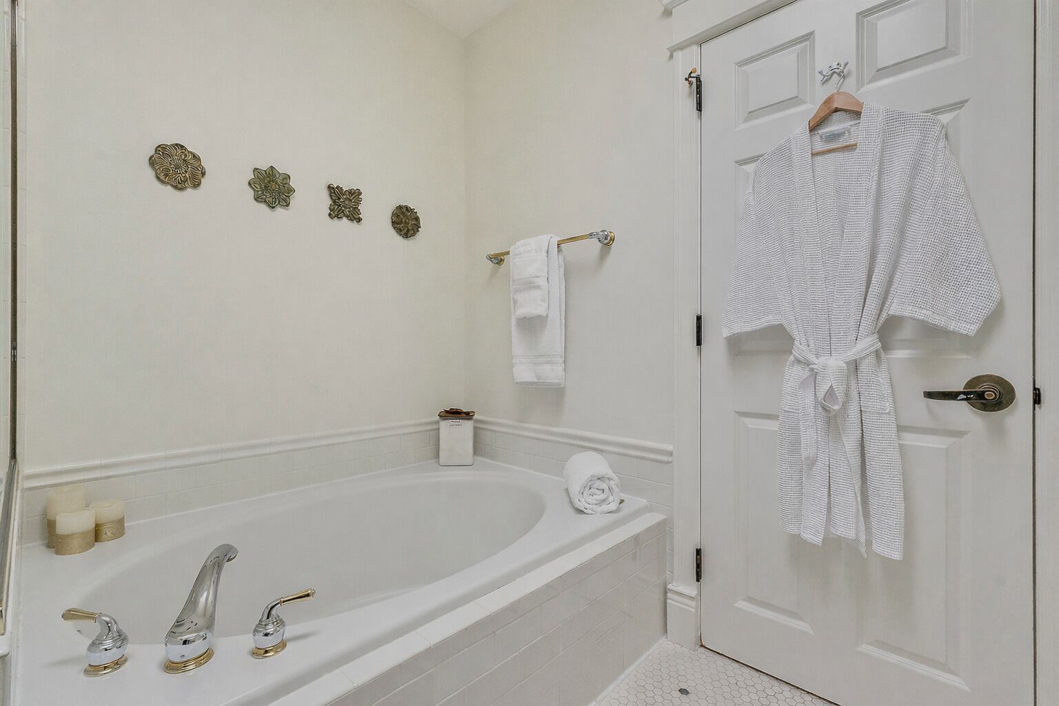 Un baño con bañera, dos grifos, un perchero para toallas y una puerta con una bata colgada.