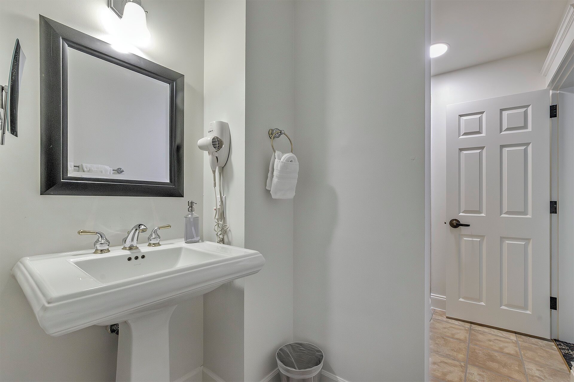 Un bagno con un lavandino bianco, uno specchio, un asciugacapelli e un portasacchi.