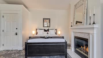 Un dormitorio con cama, chimenea, una puerta y una obra de arte enmarcada en la pared.