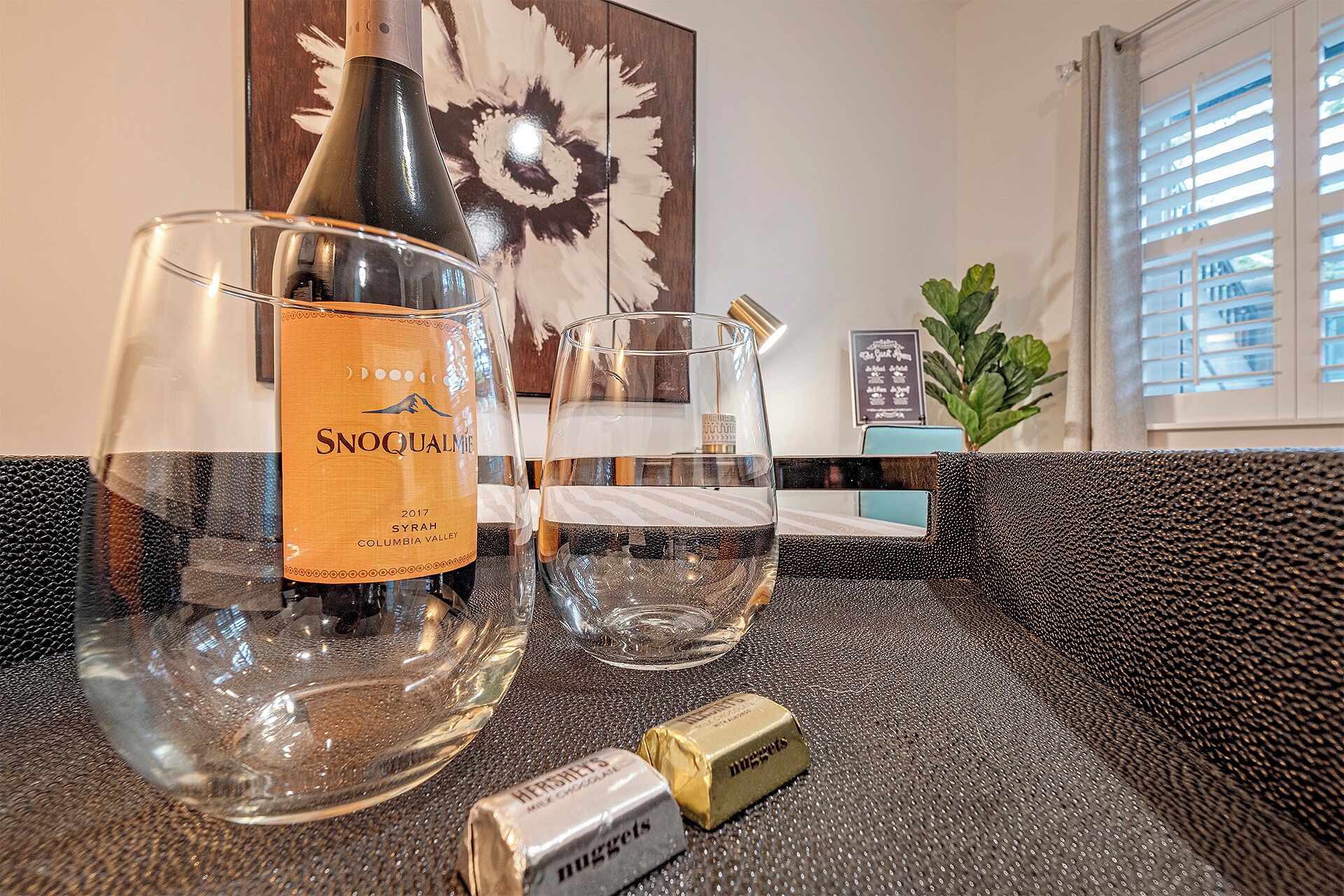 Une bouteille de vin, deux verres et une boîte de chocolats sur un comptoir à surface texturée.
