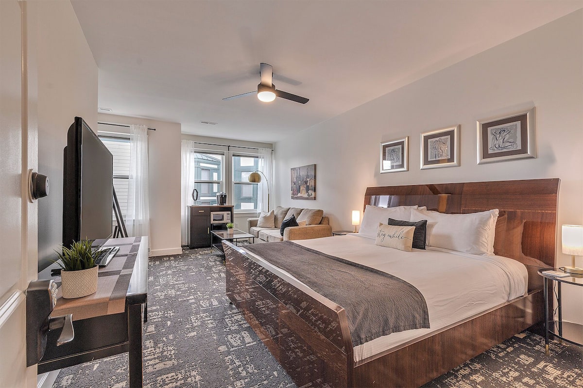 A hotel room with a bed, a desk, a chair, a ceiling fan, and artwork on the walls.