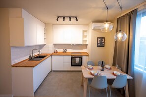 Eine moderne Küche mit weißen Schränken, einer Holz Arbeitsplatte und einem Essbereich mit Tisch für zwei Personen.