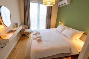 Ein Hotelzimmer mit einem Bett, einem Schreibtisch mit Lampe, einem Stuhl und einem Fenster mit Vorhängen.