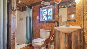 A rustic bathroom with wooden walls, a toilet, a sink, and a shower. - Surf Shack at Triple Z (Medicine Park)
