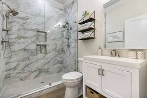 Une salle de bain moderne avec une douche à parois de verre, des toilettes blanches et un meuble-lavabo doté d’un miroir et d’étagères.