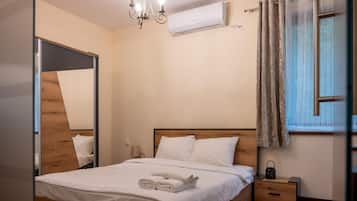 Un dormitorio con cabecera de madera, cama con sábanas blancas, mesita de noche con lámpara y un equipo de aire acondicionado.