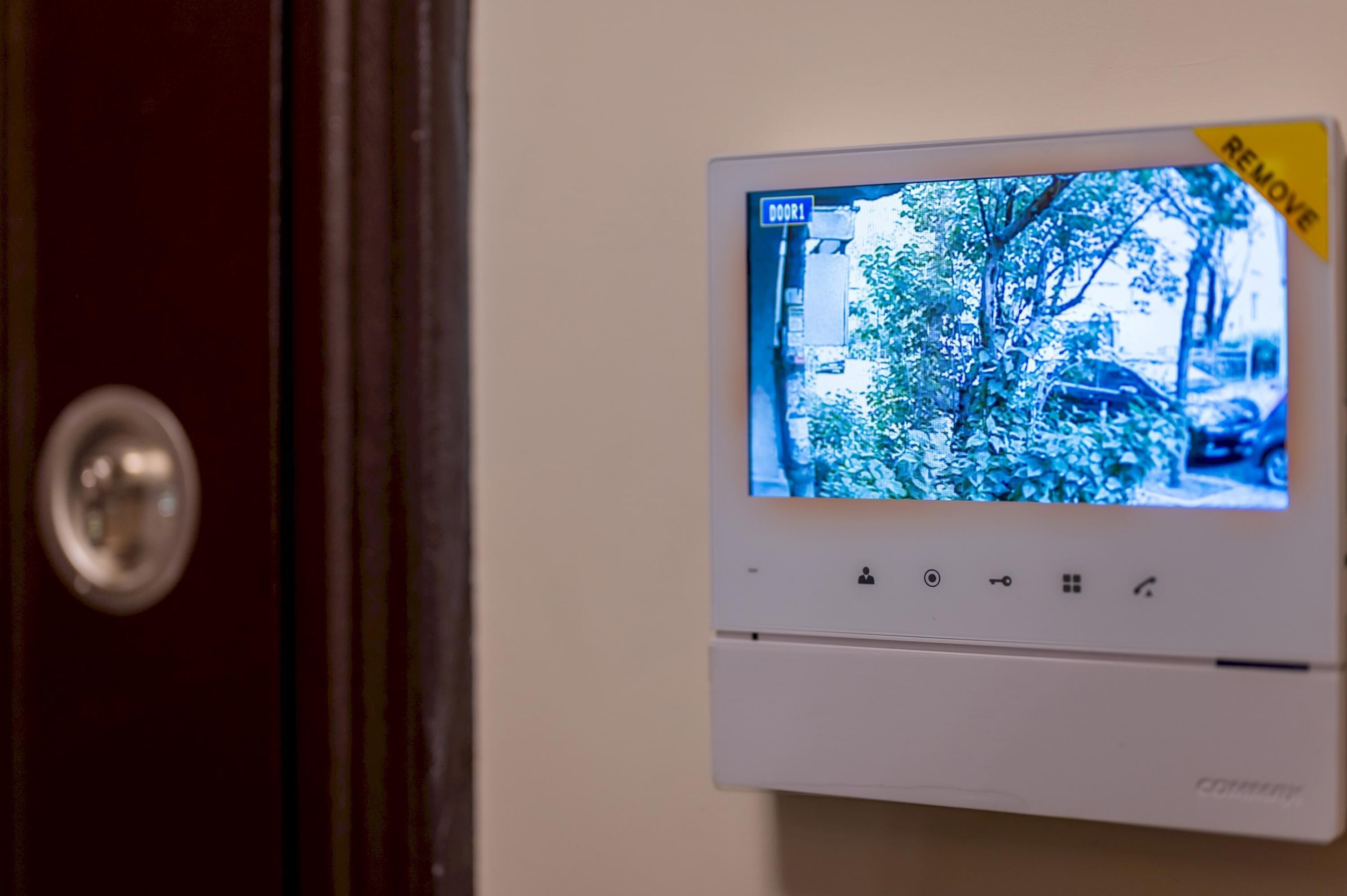 A security camera mounted on a wall, displaying a view of a street with trees and parked cars.