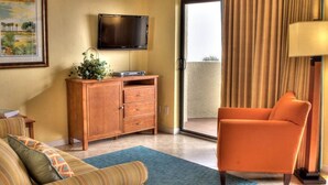 A hotel room with a sofa, a wooden cabinet, a television, a lamp, and a view through a sliding door. - Two Bedroom, Luxury Condo, Ormond Beach, FL  3973676 (Ormond Beach)