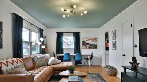 A modern living room with a brown leather sofa, a wooden coffee table, and a dining area with blue chairs. - THE GOOD PLACE - Walk to Uptown Westerville - 3BR (Westerville)