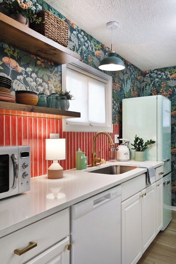 A kitchen with a white countertop, a red-striped backsplash, a vintage-style refrigerator, and a hanging light fixture.