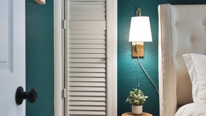 A bedroom with teal walls, a white door, a wooden chair, a bedside table with a lamp, and a bed with white bedding. - THE GOOD PLACE - Walk to Uptown Westerville - 3BR (Westerville)